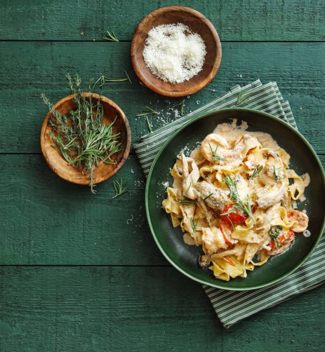 Italian fettuccine with prawns, salmon and herbs. Flat lay top-down composition on dark green background.